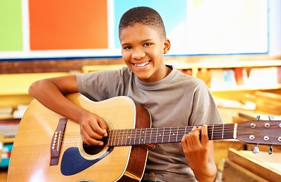 child with a smile holding a 
                guitar
